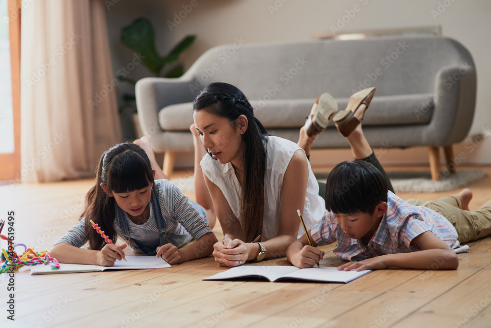 Mom makes sure that the kids do homework. Shot of a cheerful mother and her two children doing homework together while lying on the floor at home during the day.
